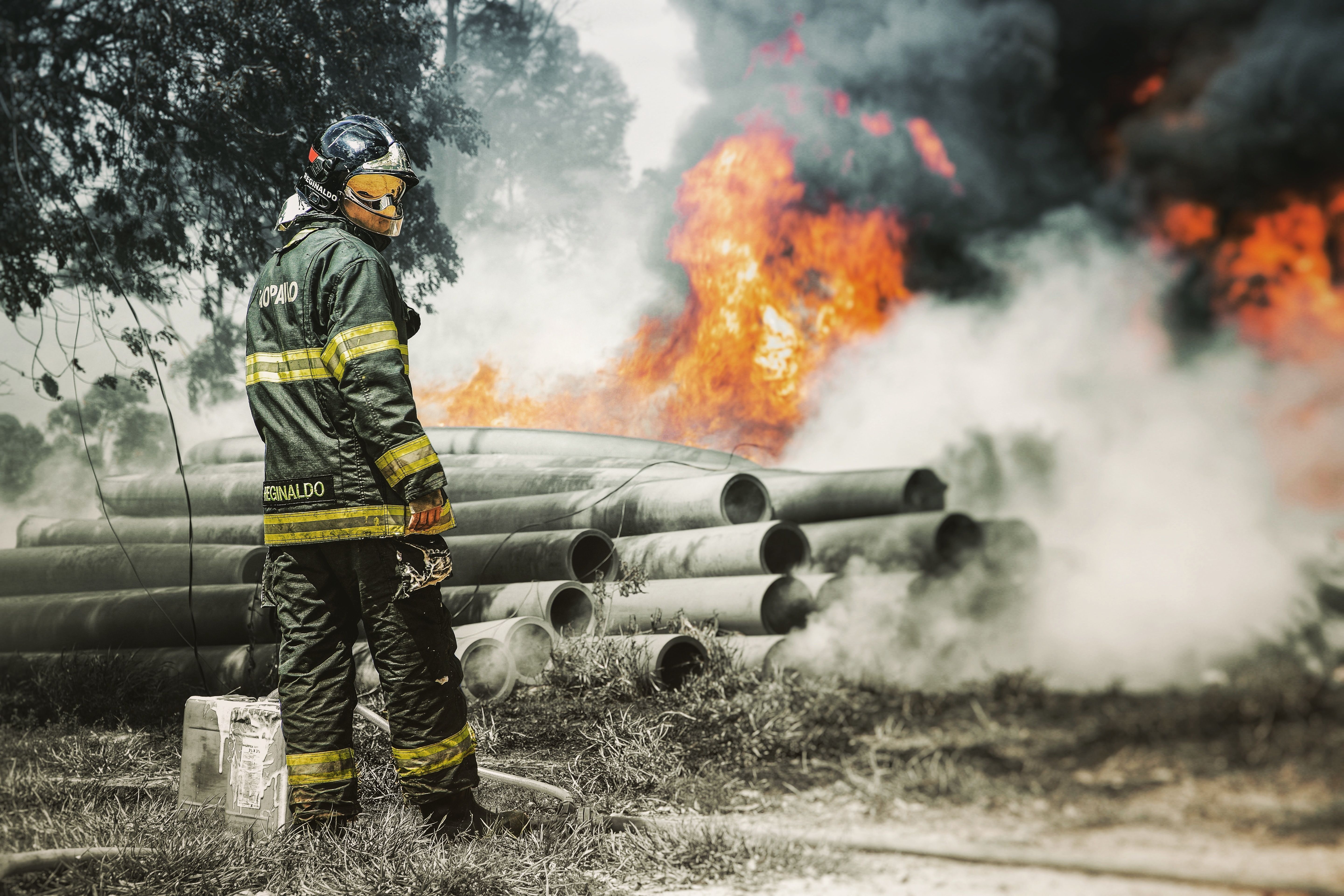 Un bombero equipado frente a un foco de fuego y humo.